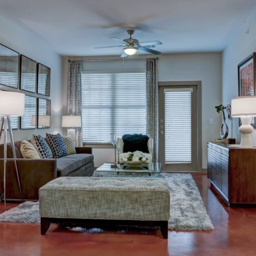 Model apartment living room with couch, ceiling fan, and door to patio/balcony