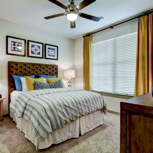 Model apartment carpeted and furnished bedroom with ceiling fan