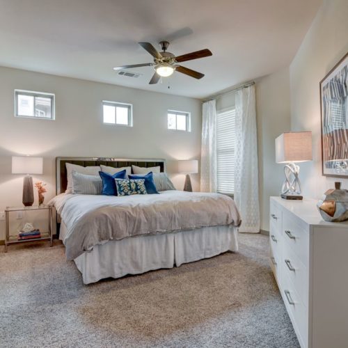 Model apartment furnished carpeted bedroom with ceiling fan, bed, and dresser